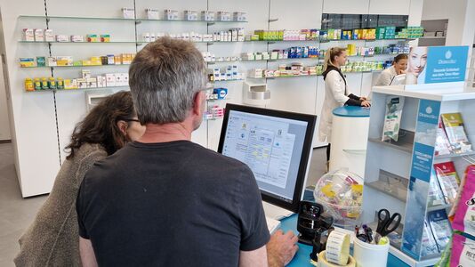 Personen im Gespräch in einer Apotheke vor dem Computer